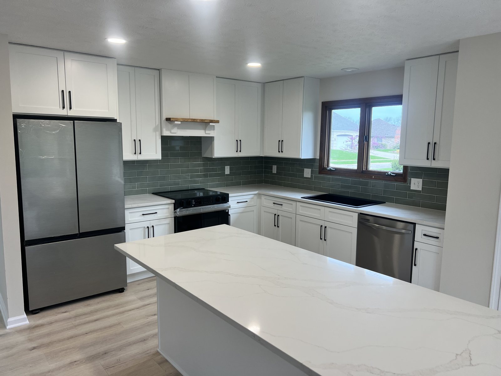 Finished kitchen with white shaker cabinets, green glass subway tile backsplash, quartz island, and light plank floors