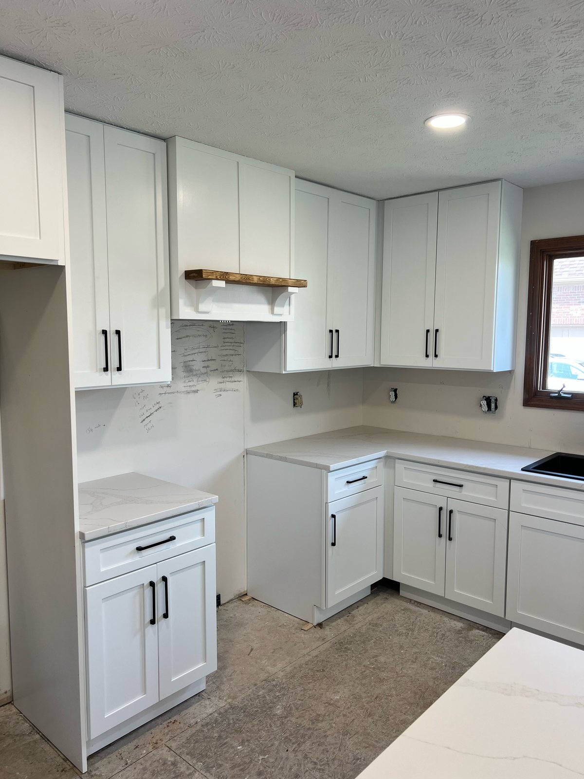 White quartz countertops and wood range hood shelf installed on white shaker cabinets, before backsplash and flooring