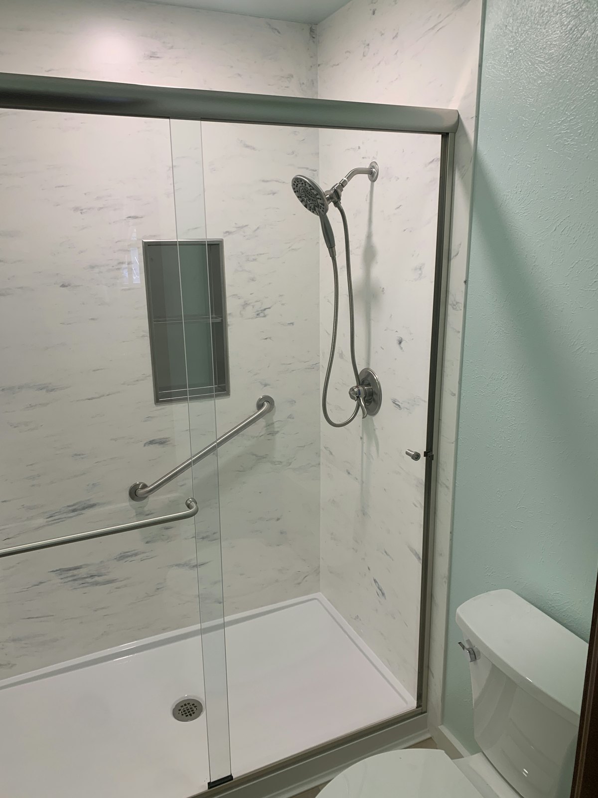 Alcove-size walk-in shower with a low-threshold base, sliding glass door, grab bars, and recessed niche