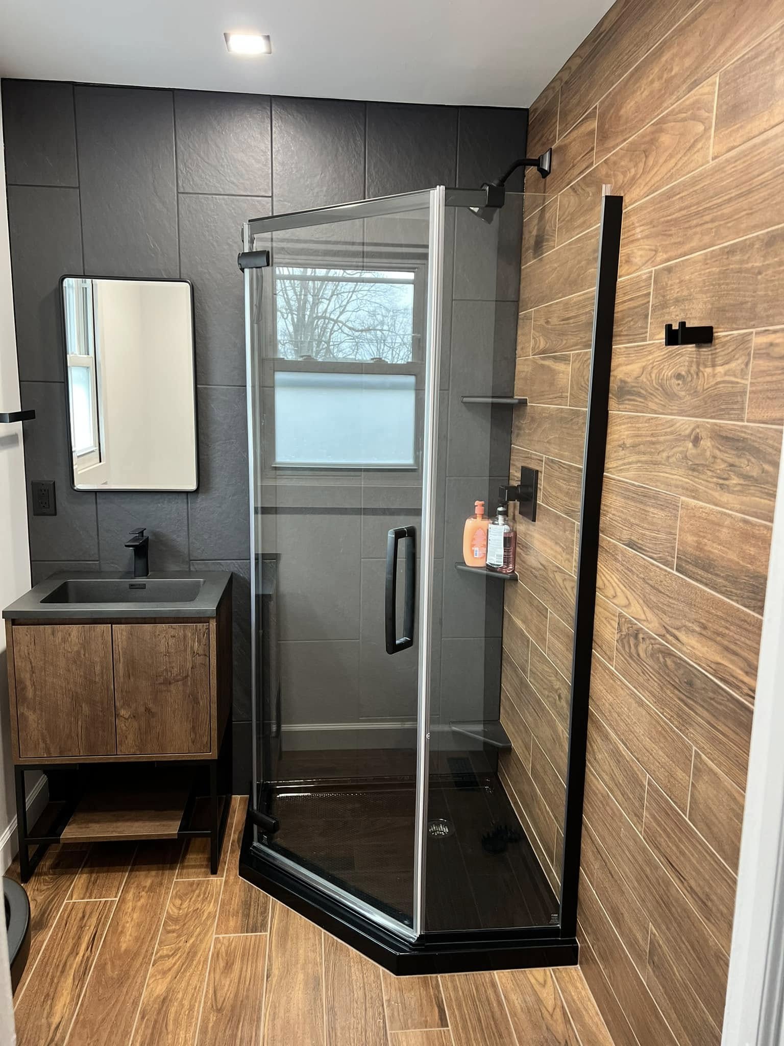 Neo-angle glass shower with wood-look plank tile, charcoal slate-look wall tile, and matte black fixtures