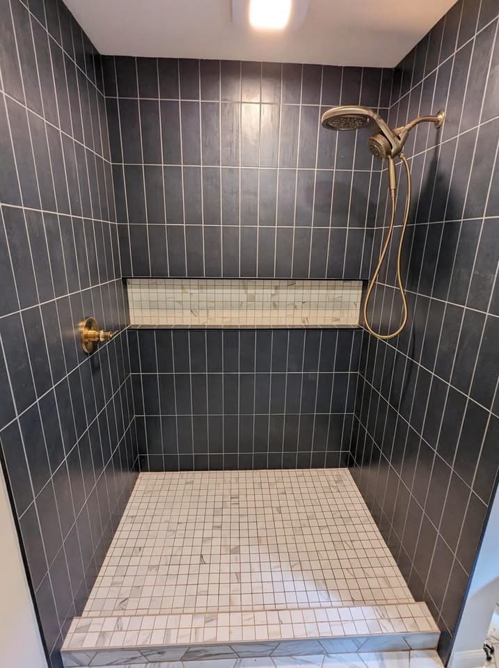 Walk-in shower with charcoal vertical stacked tile, white marble-look mosaic floor and niche, and brushed gold fixtures