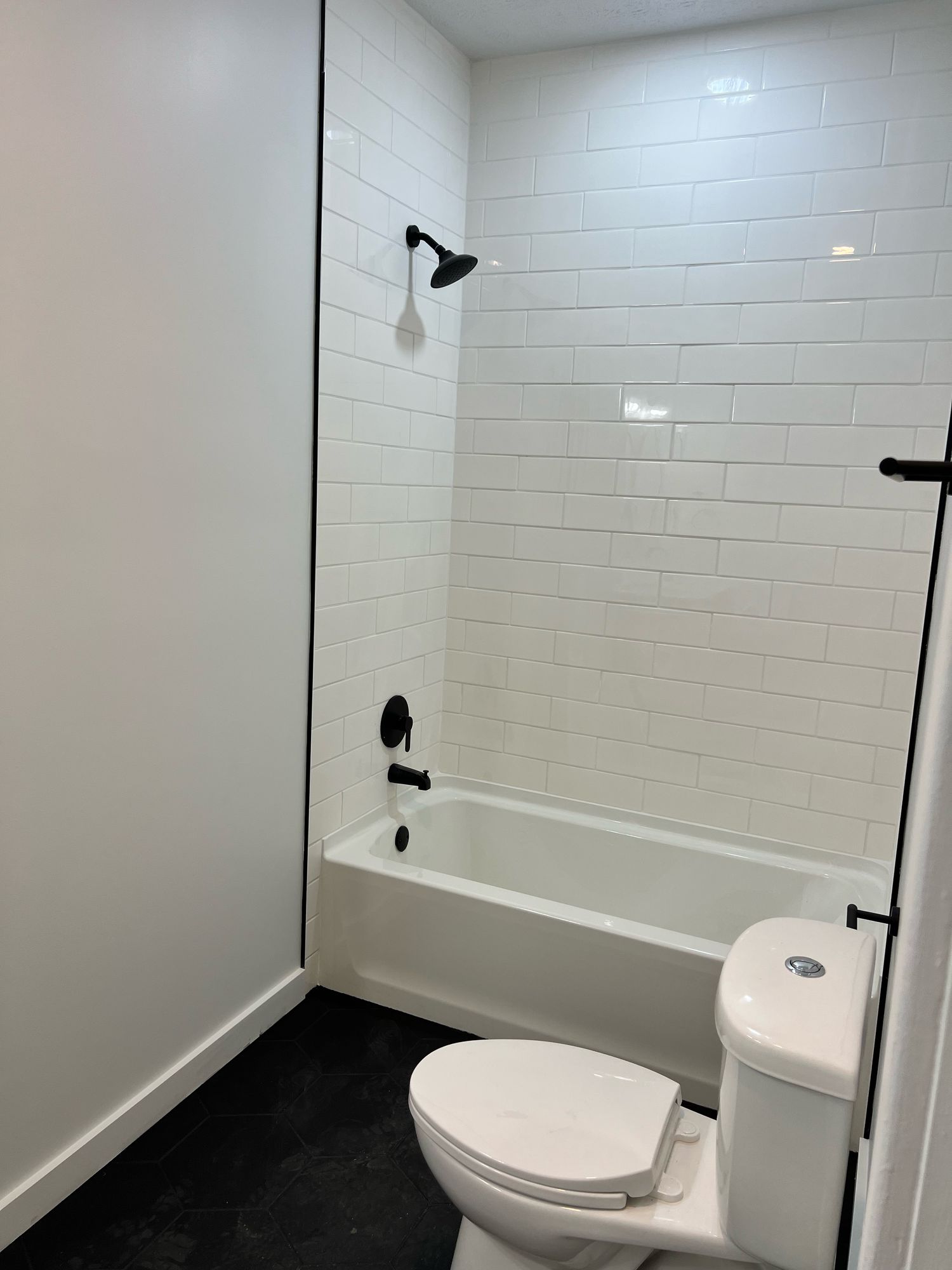 Tub-shower with white subway tile to the ceiling, a matte black shower head and valve, and matte black hexagon floor tile