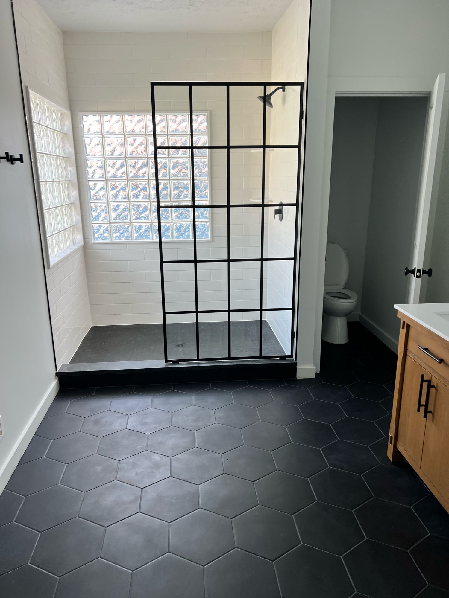 Walk-in shower with white subway tile, glass block windows, a matte black grid glass screen, and a black hex tile floor