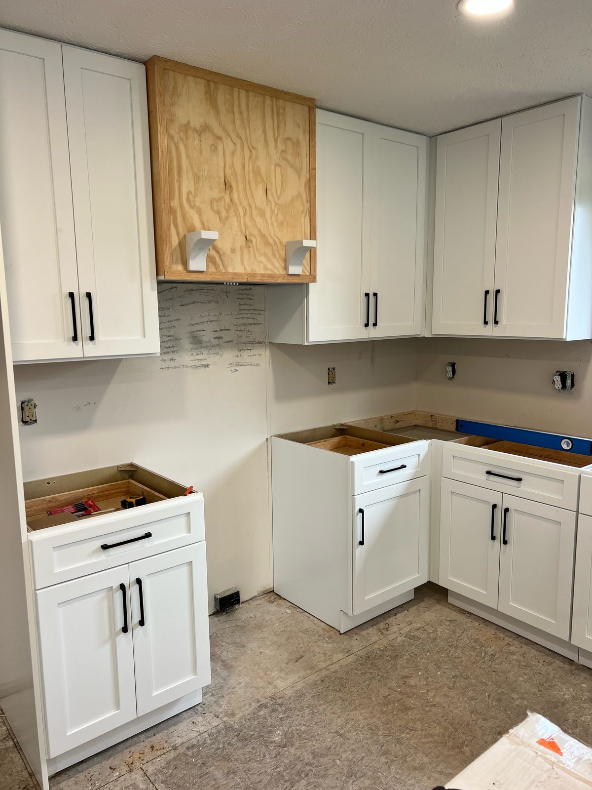 White shaker kitchen cabinets with matte black pulls installed before countertops