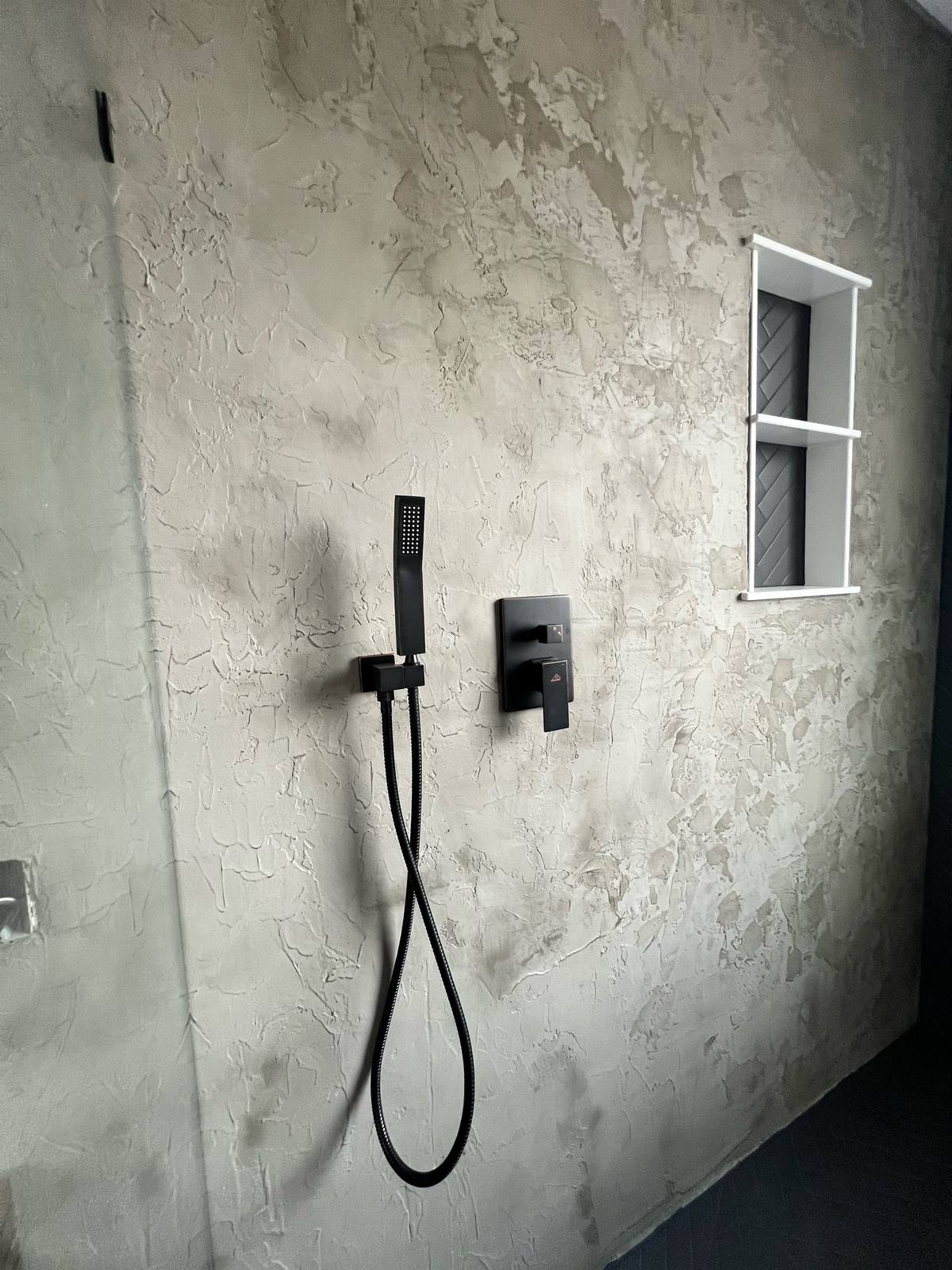 Shower with textured plaster walls, matte black handheld shower and valve, and recessed white niche