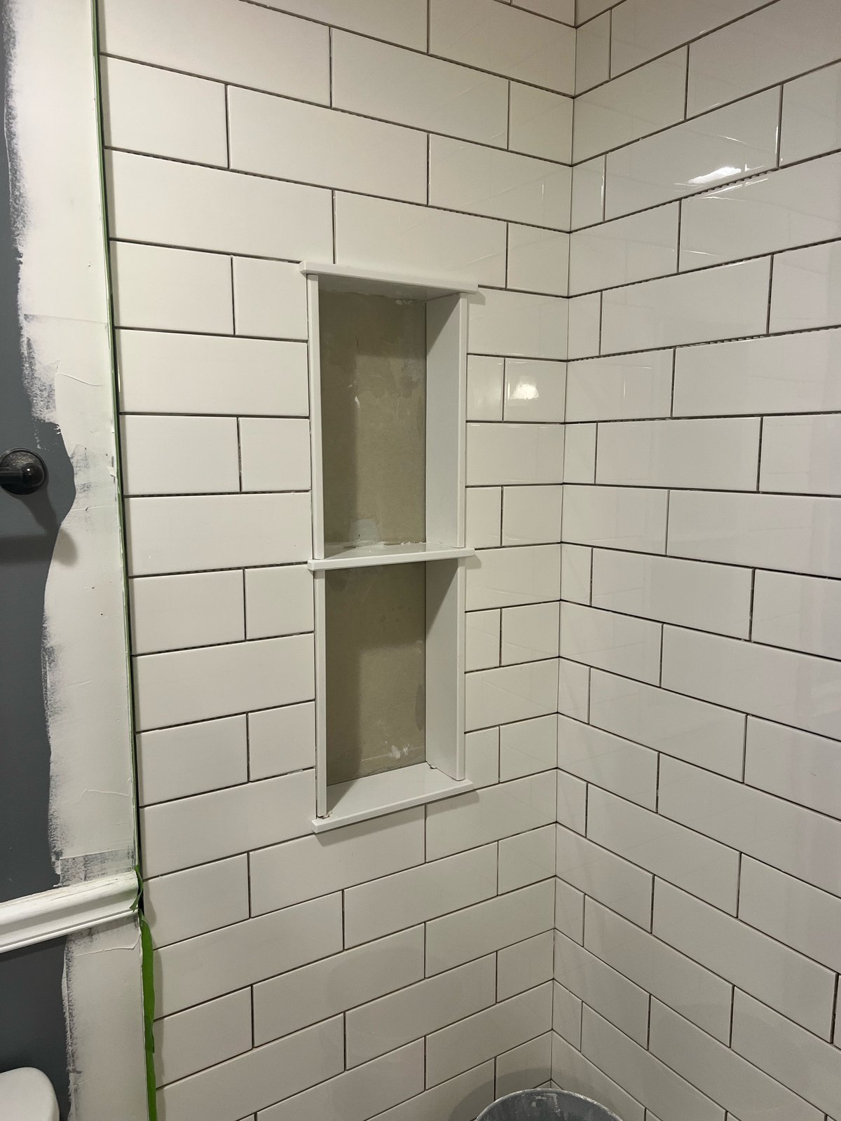 White subway tile shower with dark grout and two-shelf niche, mid-install